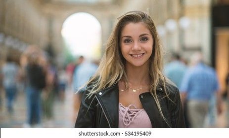 Jeune fille souriante portant une veste en cuir noire dans une galerie.